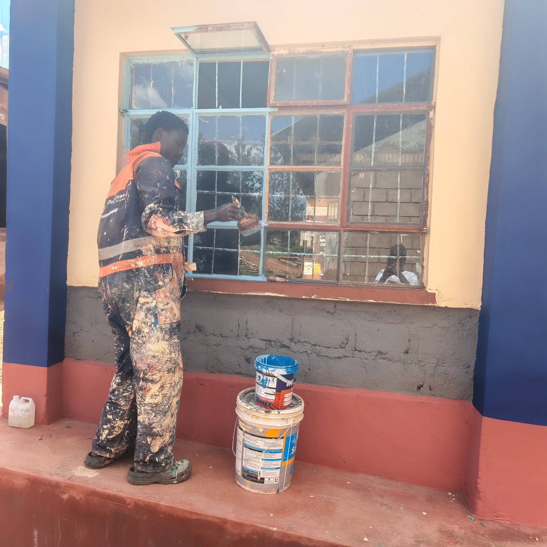 Painter brushing light blue paint onto a large classroom window frame