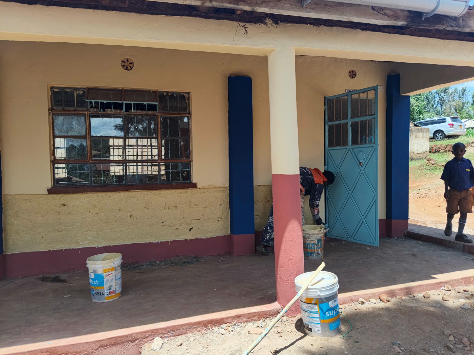 Painter working along a repainted classroom veranda with pupils passing by