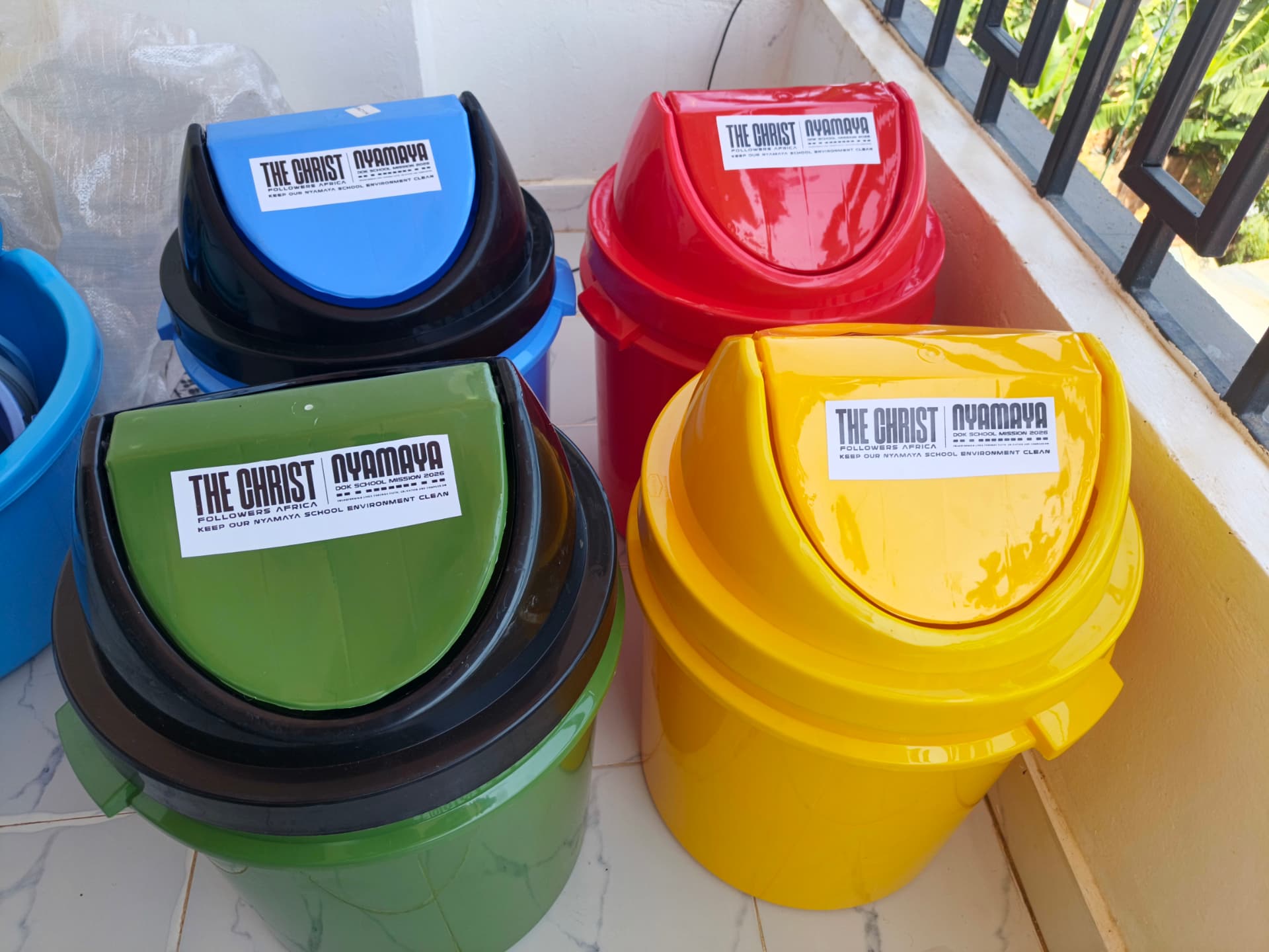 Colourful push-top waste bins labelled The Christ Nyamaya DOK School Mission 2026
