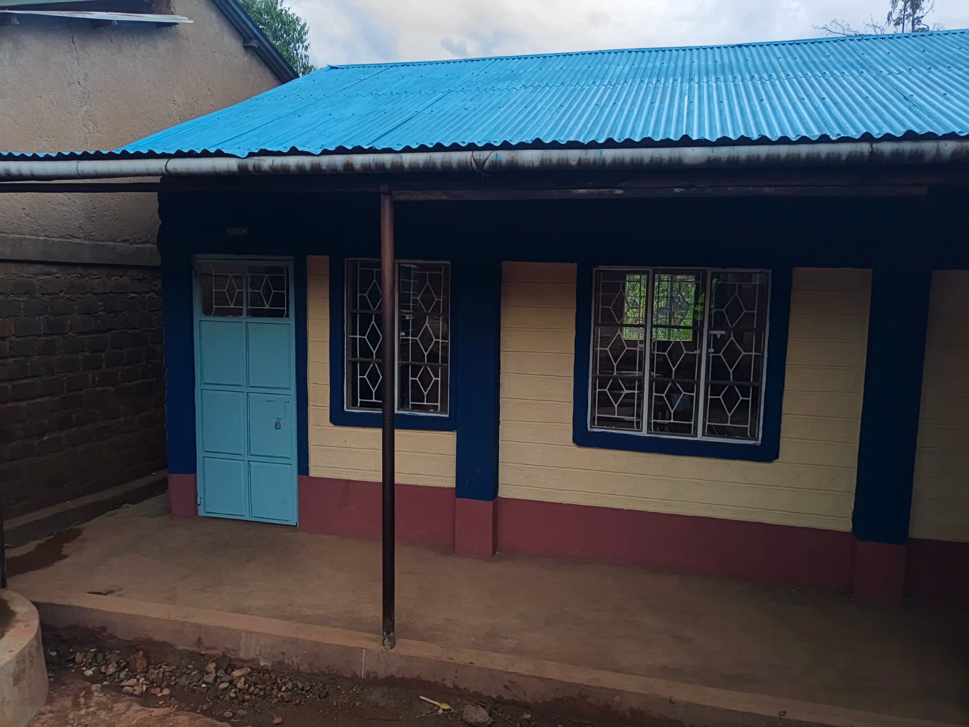 Classroom entrance under a new blue iron roof with painted door and windows