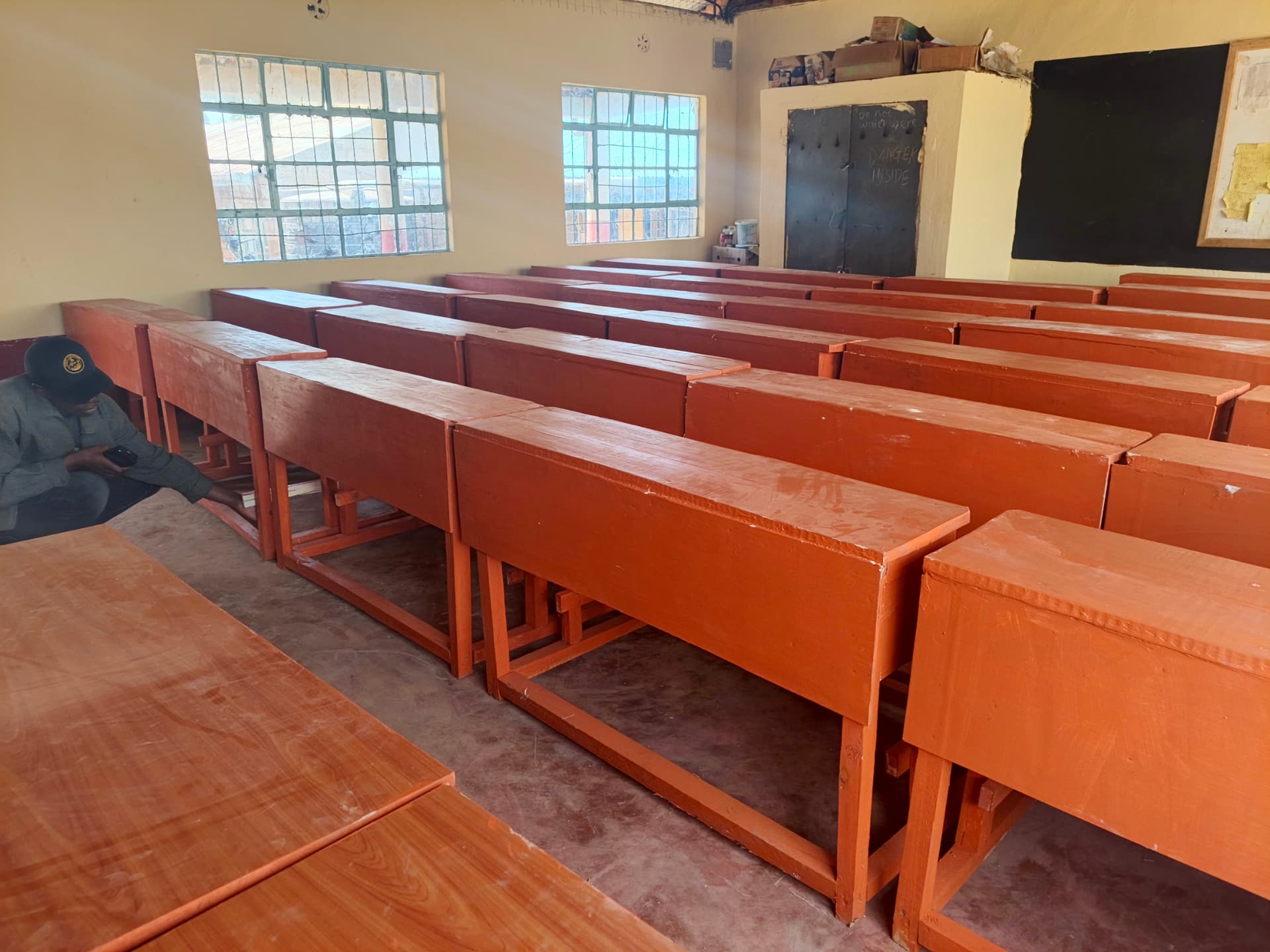 Rows of varnished wooden desks in a classroom with a pupil seated nearby