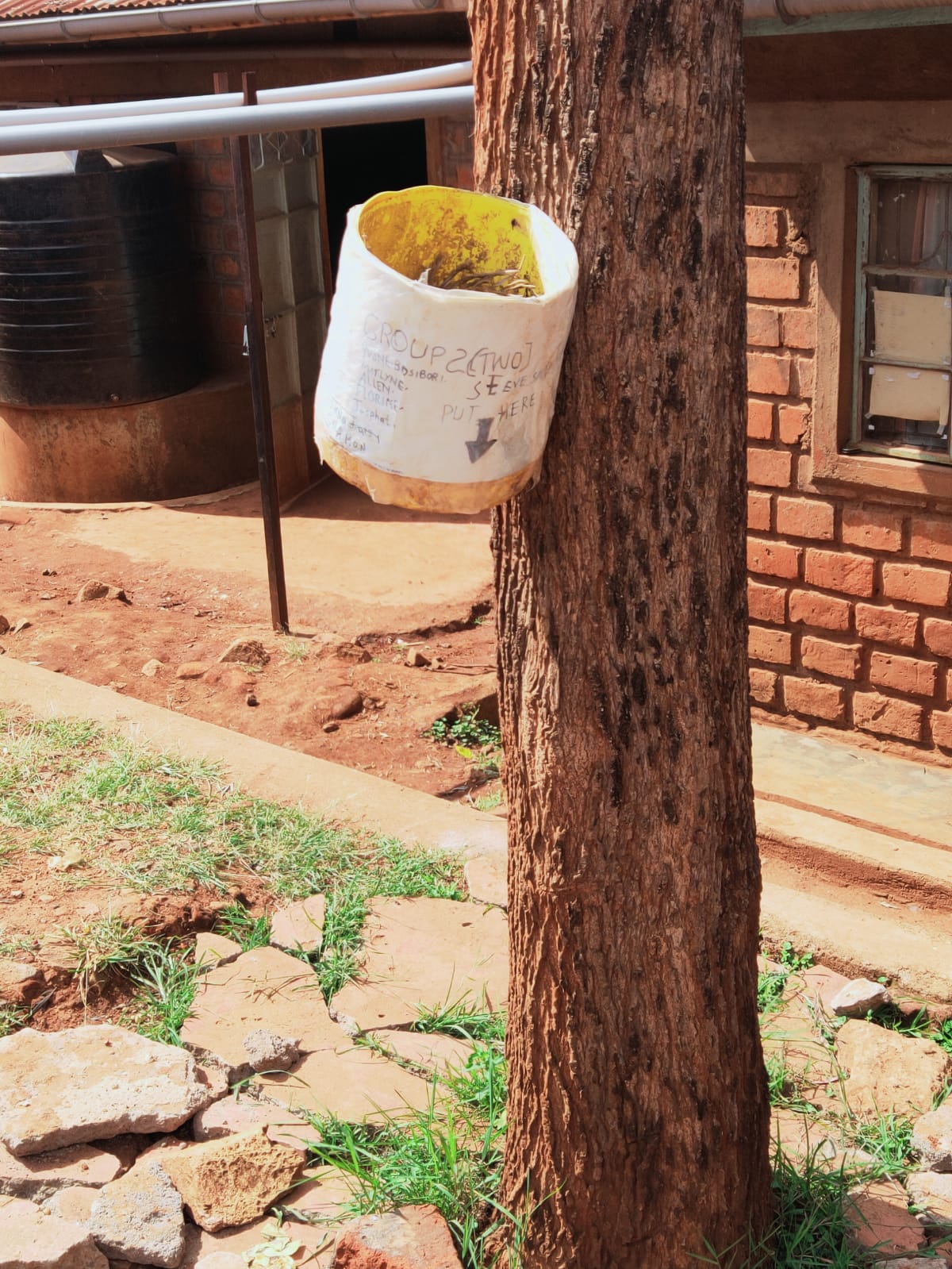 Old plastic container tied to a tree serving as a makeshift dustbin