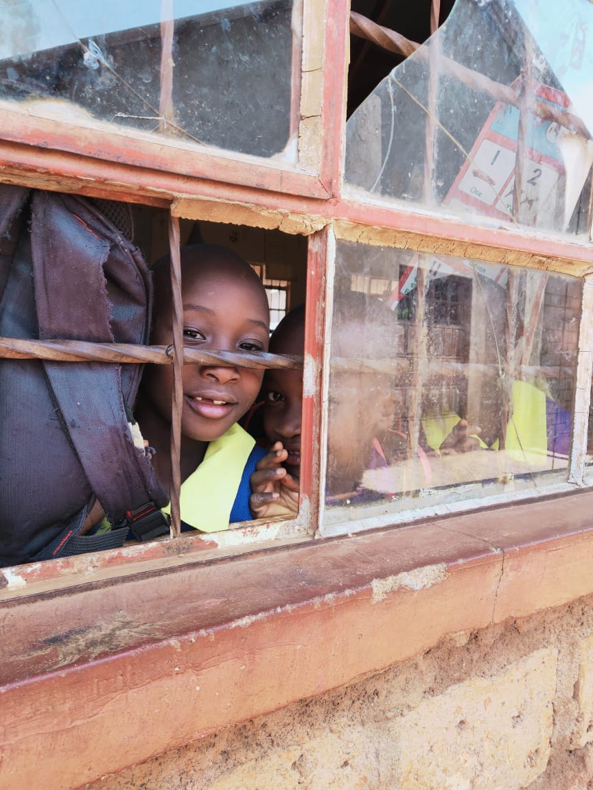Pupils peeking through a broken classroom window frame
