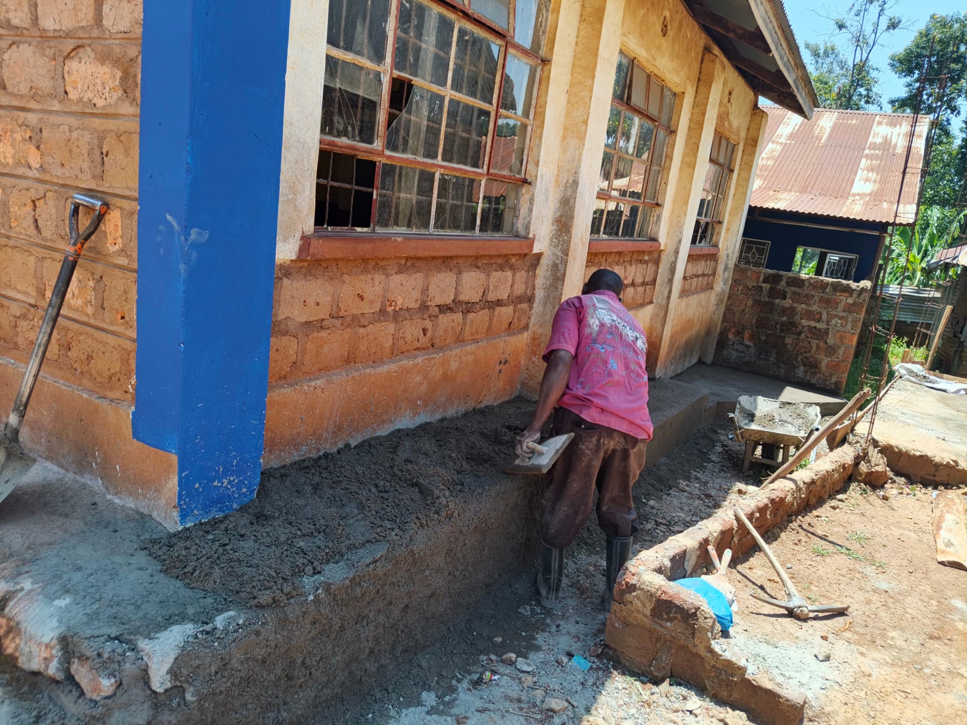 Mason plastering a new concrete apron beside the classroom block