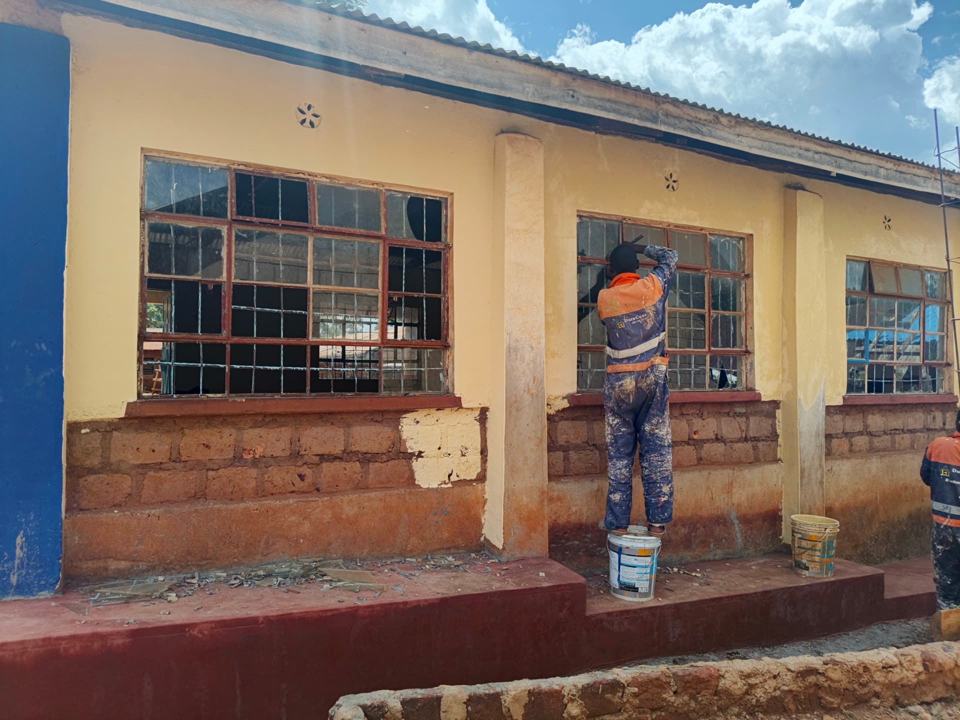Workers repairing classroom window frames from paint buckets